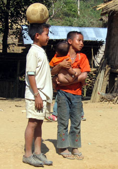 In Laos, a boy carries his little brother while his friend balances a ball.